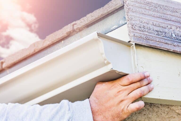 Worker Attaching Aluminum Rain Gutter to Fascia of House.